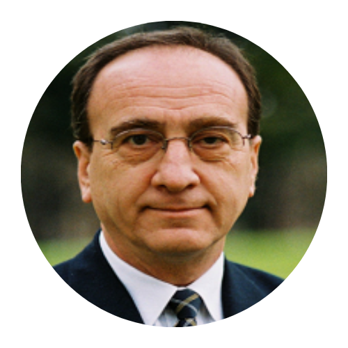 Portrait of a man in glasses and a dark suit against a blurred outdoor background