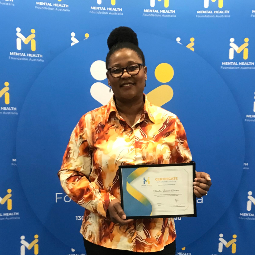 Woman holding a framed certificate in front of a blue Mental Health backdrop