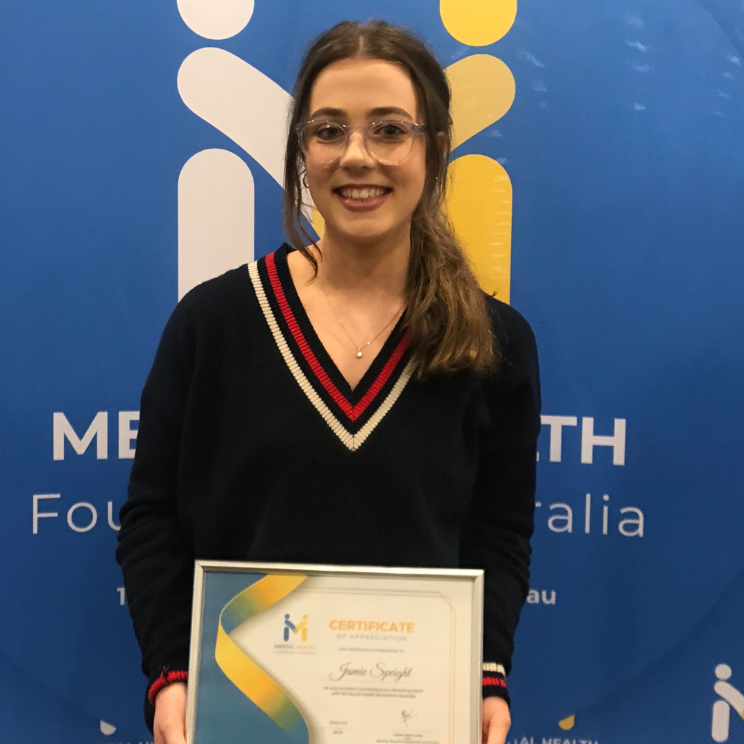 Woman in black sweater holding a certificate, smiling in front of a blue event backdrop.