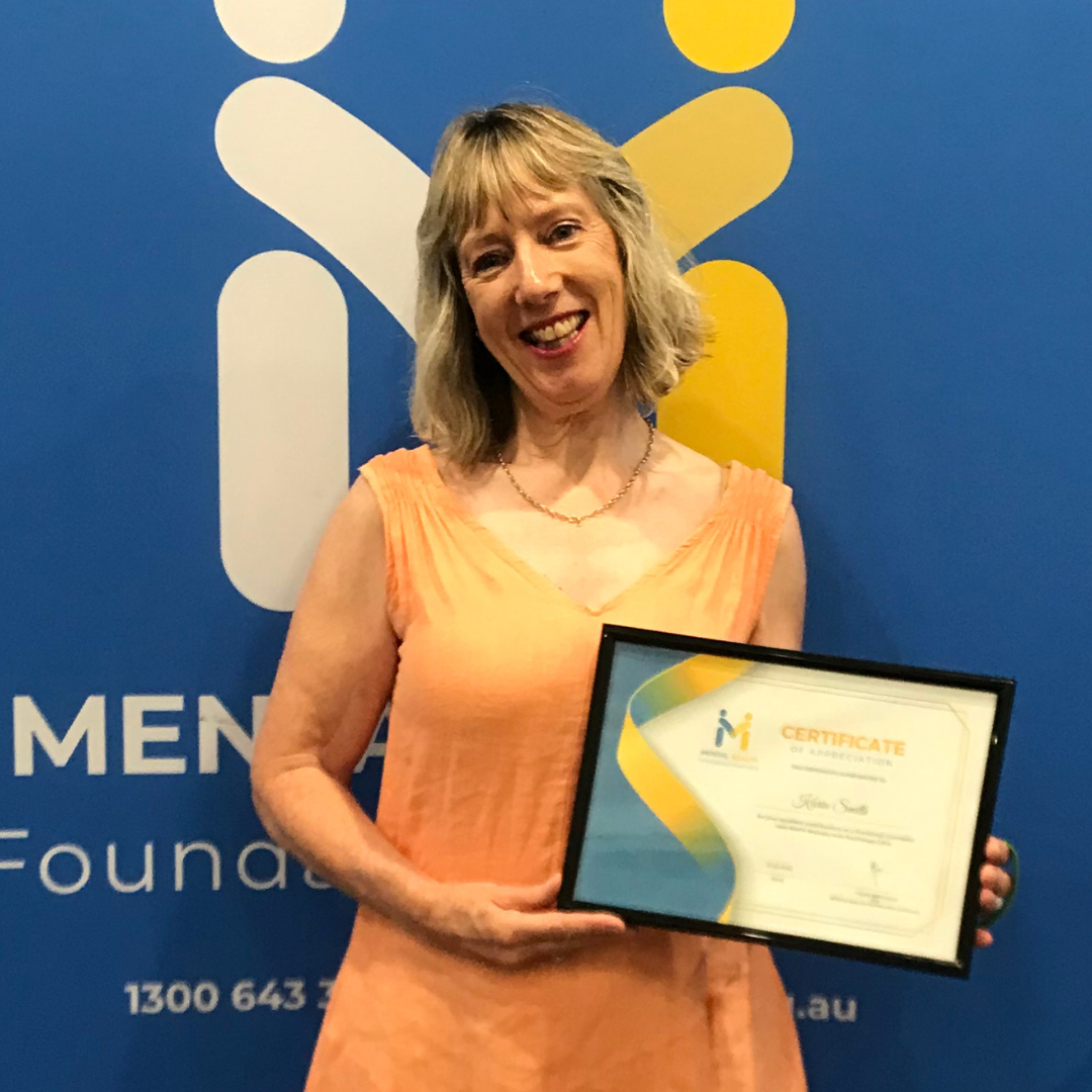 Woman in peach dress holding a framed certificate in front of a blue awards backdrop
