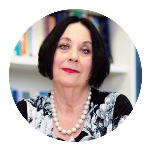 Woman with short dark hair and pearl necklace, posing in front of a blurred bookshelf background