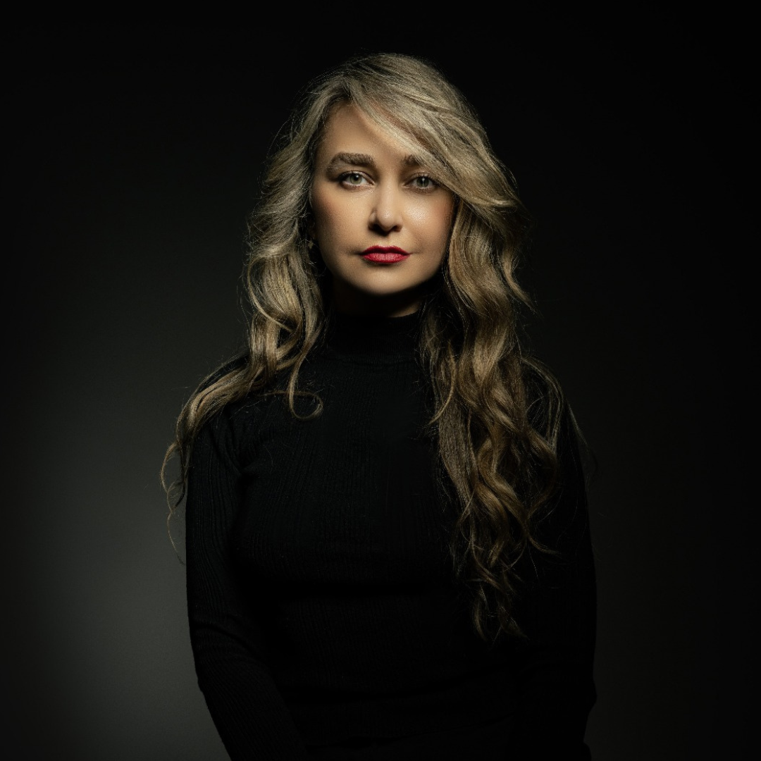 Studio portrait of a woman in a black turtleneck, with long wavy hair against a dark background