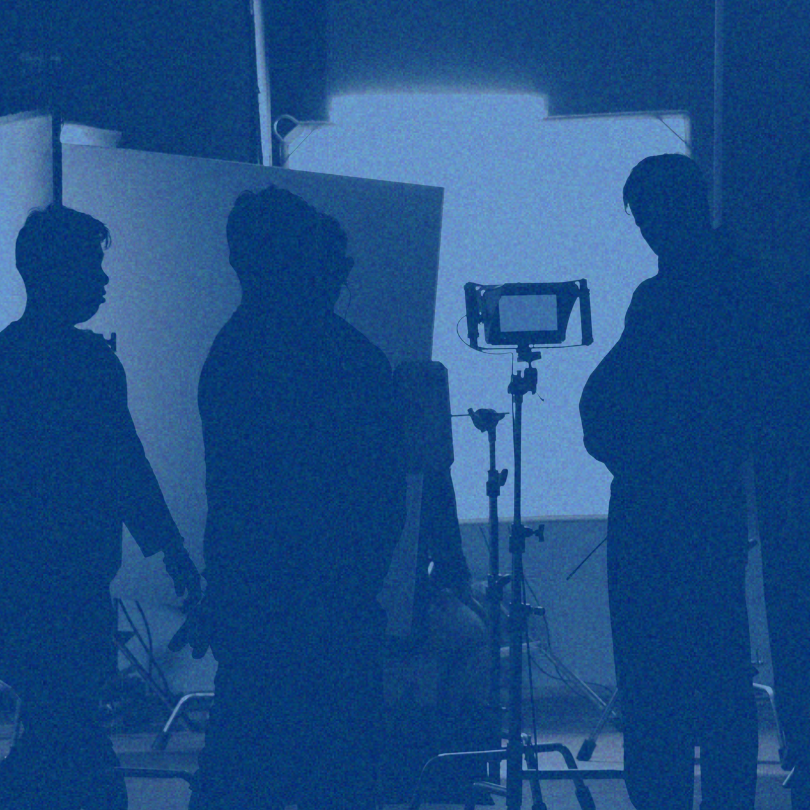 Silhouetted people stand around a camera and light in a blue-lit studio set