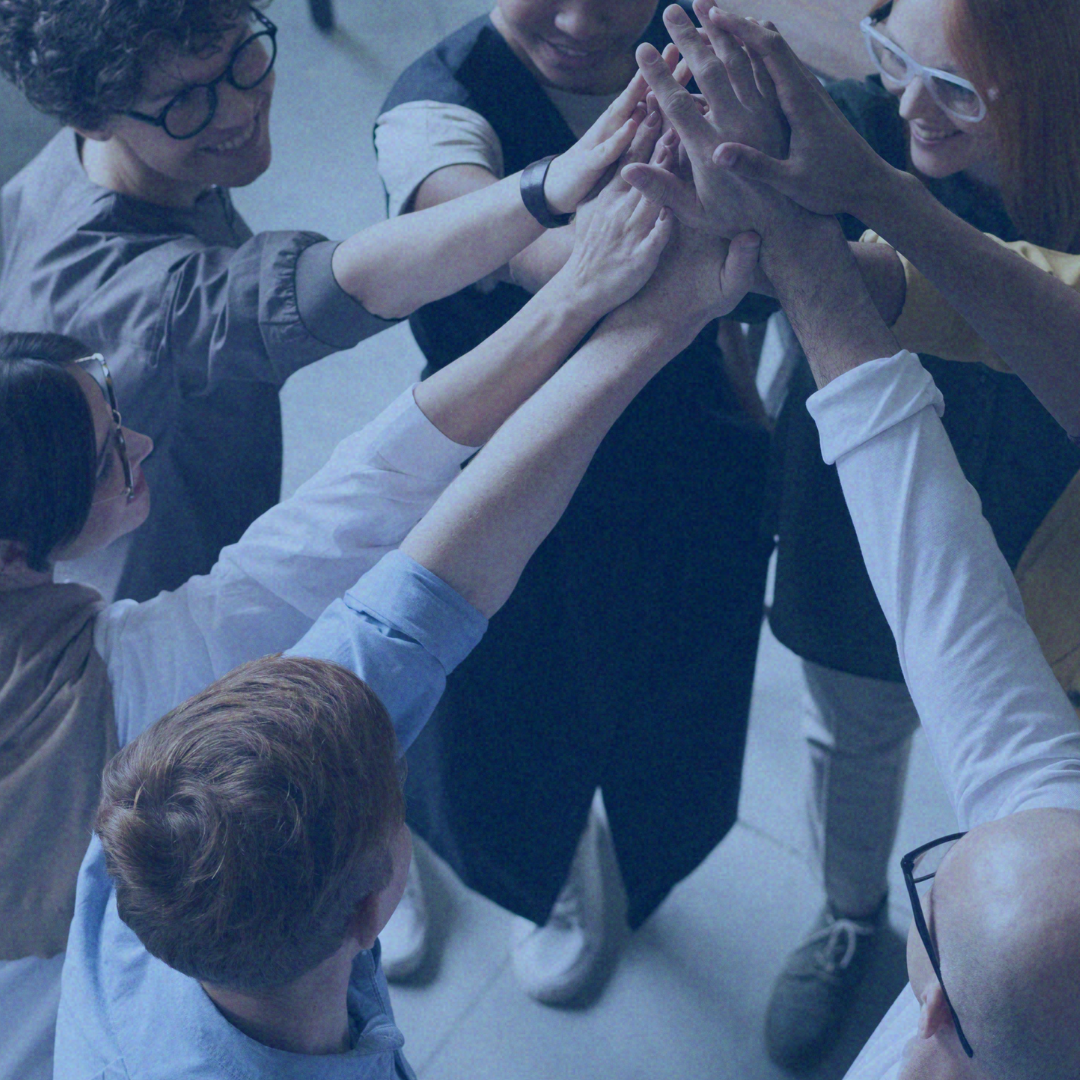 Group of coworkers stacking hands together in a team huddle in an office setting