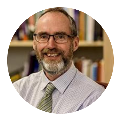 Smiling bearded man in glasses and a tie in an office with bookshelves in the background