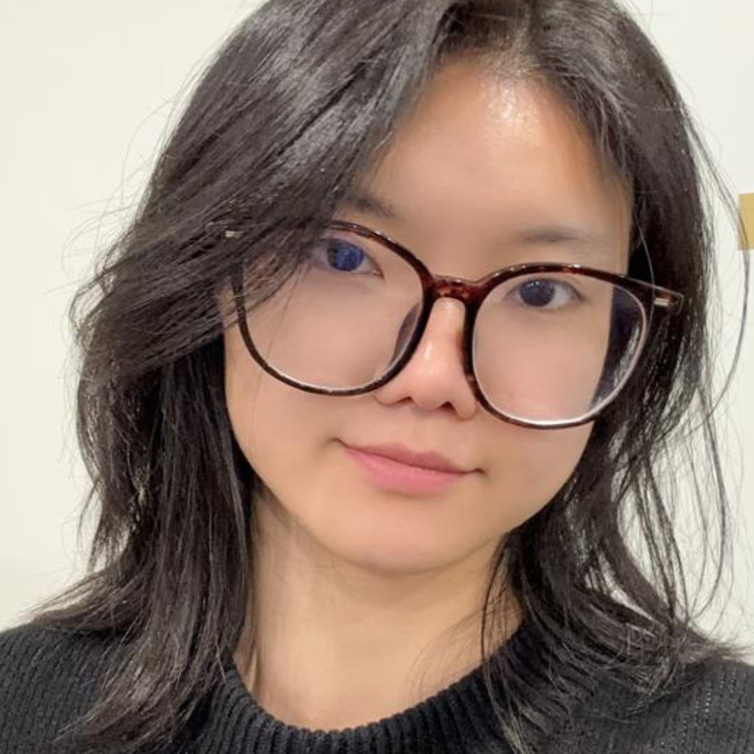 Close-up portrait of a person with dark wavy hair and large round glasses, wearing a black sweater.