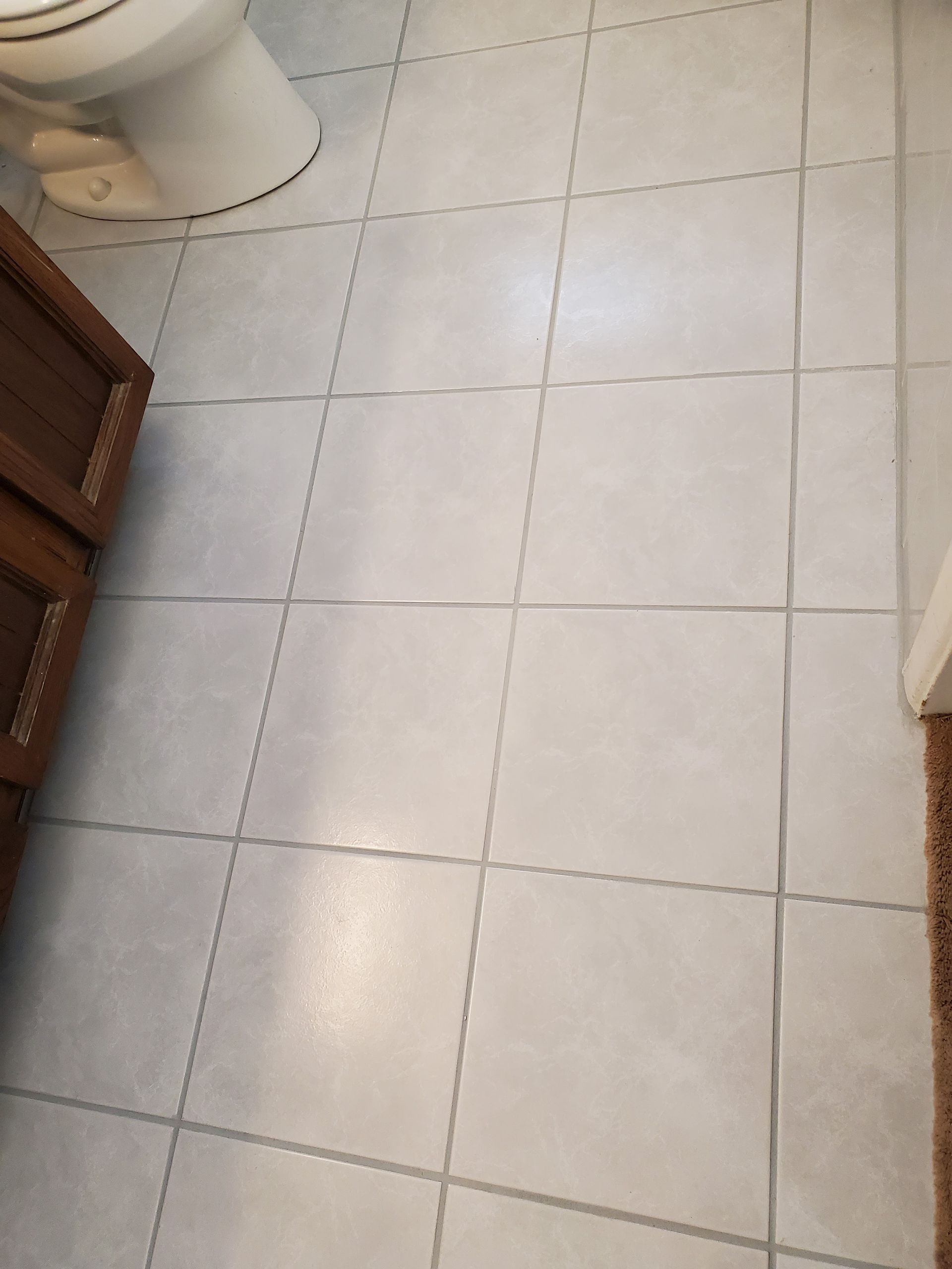 A bathroom floor with white tiles and a toilet.