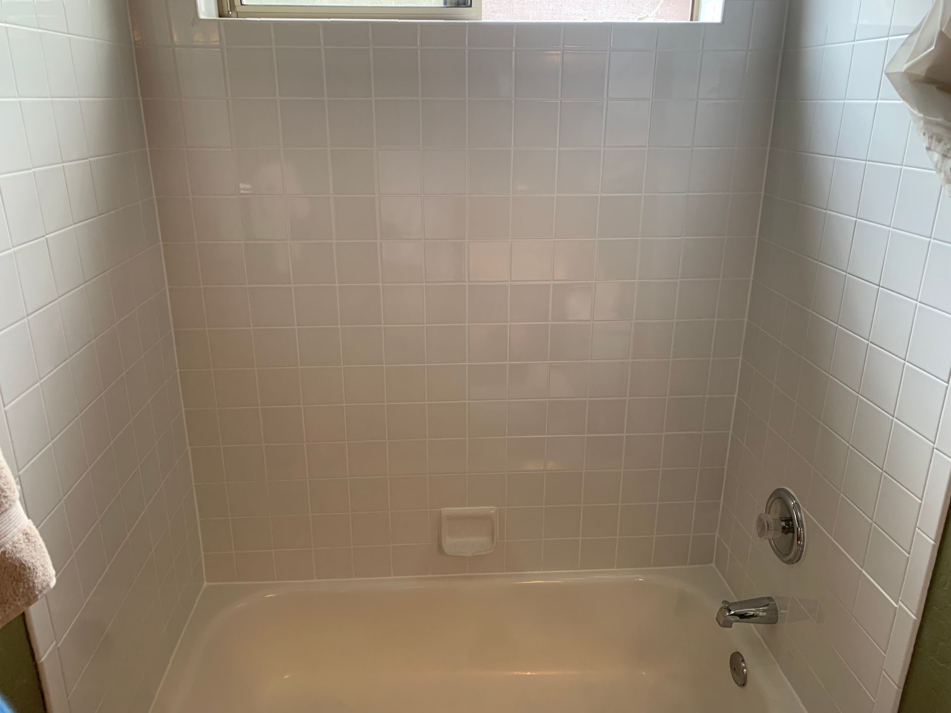 A bathtub in a bathroom with white tiles and a window.