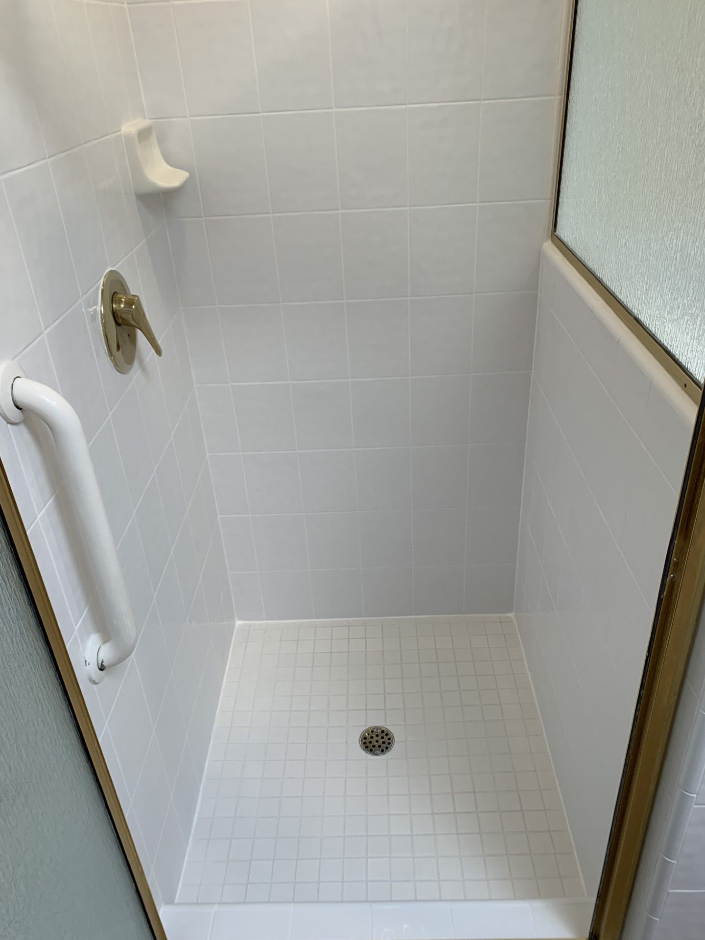 A shower stall with white tiles and a white handle.