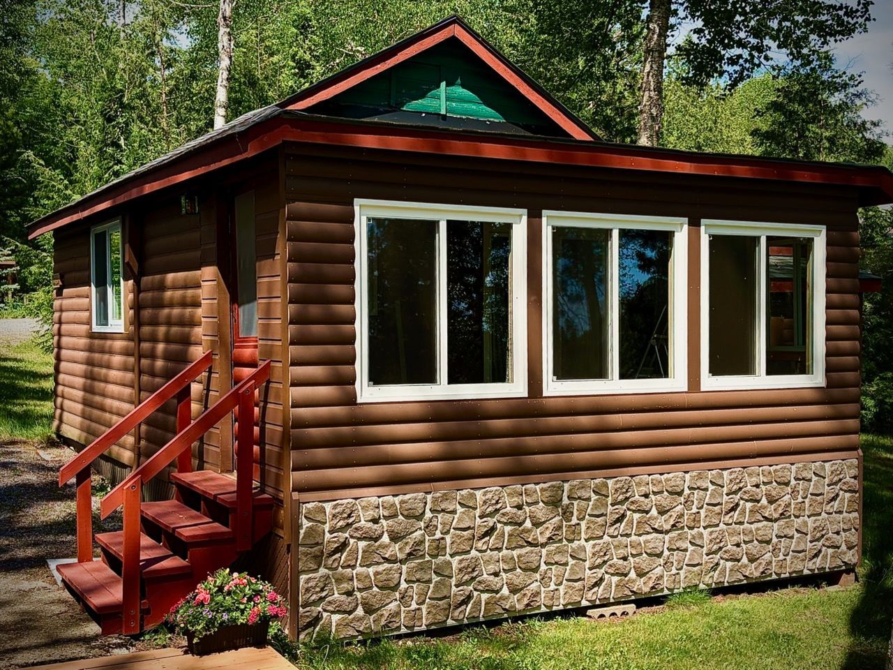 Evergreen cottage with a screened-in porch is surrounded by trees.