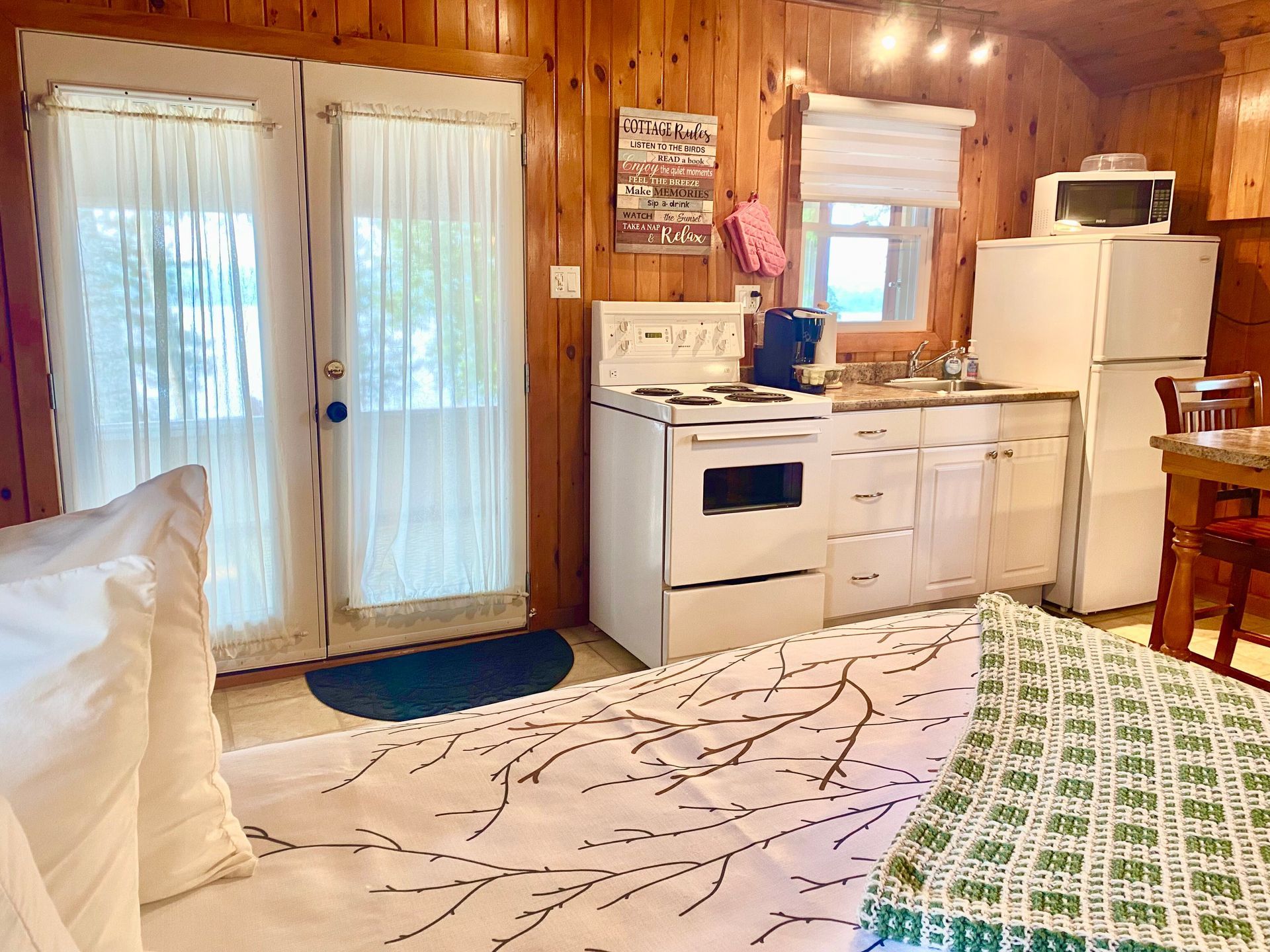 Evergreen cottage bedroom with a bed, stove, refrigerator, and microwave.