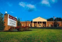 A brick funeral home and crematory building under a bright blue sky, with a prominent sign in the foreground.