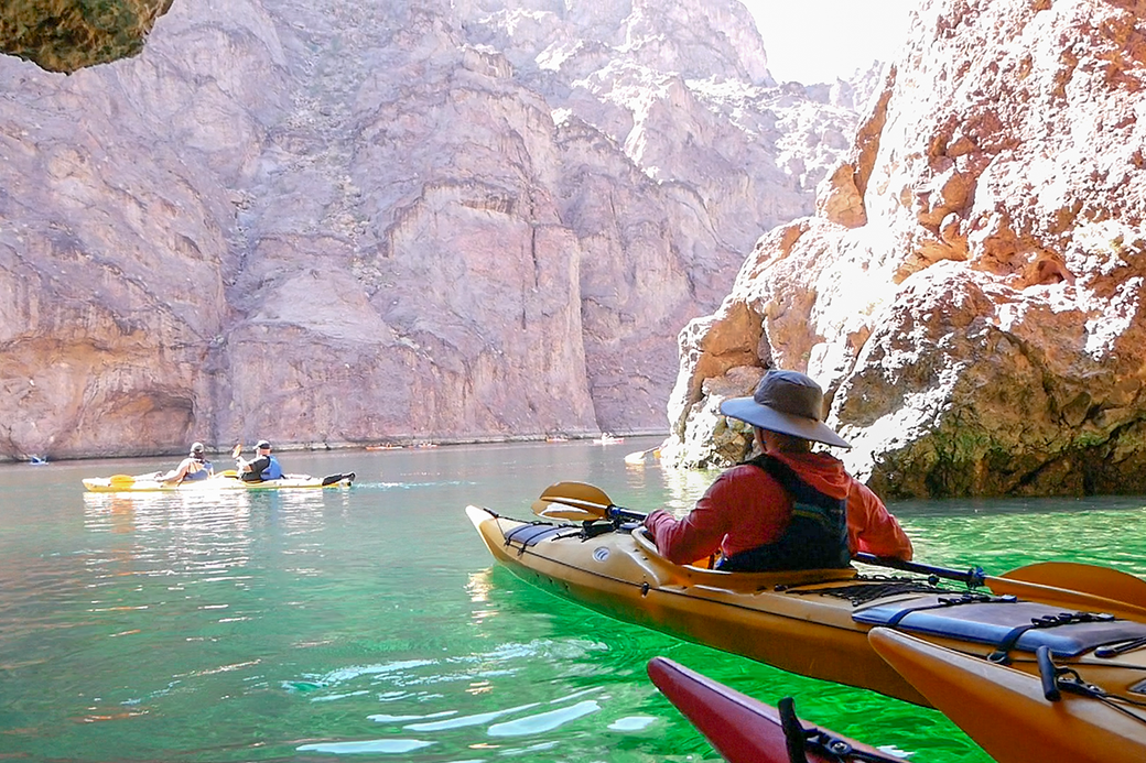 A man in a hat is sitting in a kayak on a lake.