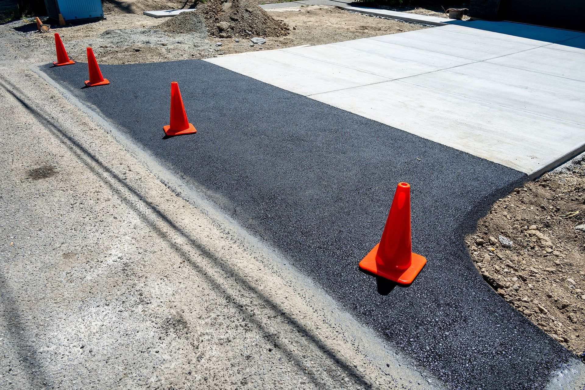 Orange traffic cones marking a fresh black asphalt strip beside a concrete driveway