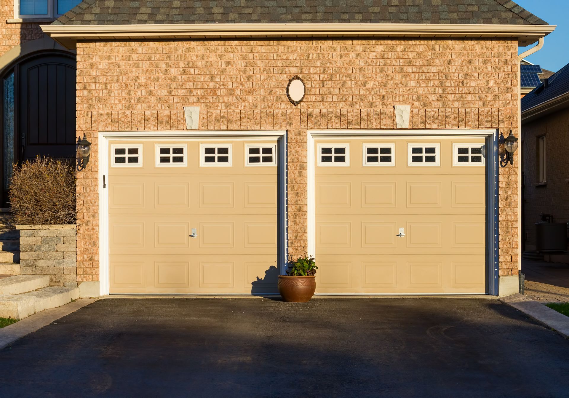 Two beige garage doors on a brick house, with a potted plant centered between them.