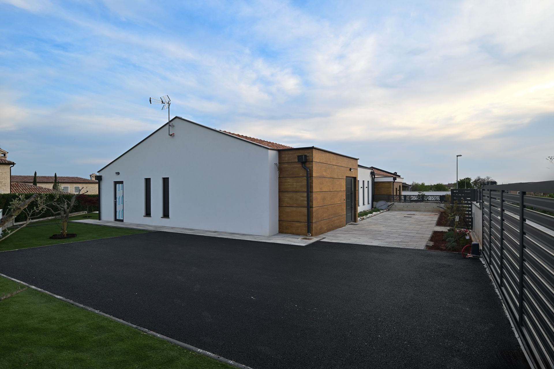 Modern white building with wood accents beside a paved driveway and grassy yard at dusk