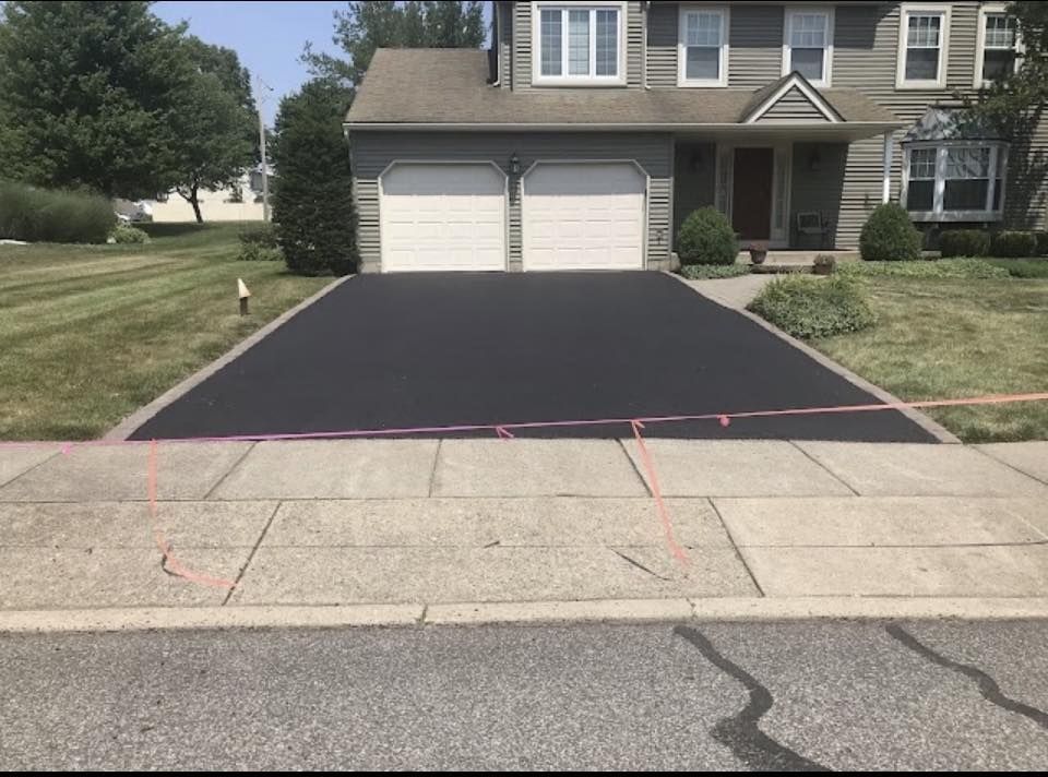 Fresh black asphalt driveway leading to a two-car garage in front of a suburban house.