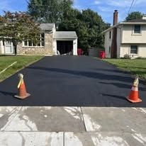 Freshly paved driveway between two houses, with orange cones at the curb entrance
