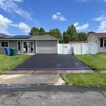 Single-story house with a new black driveway and white fence under a blue sky