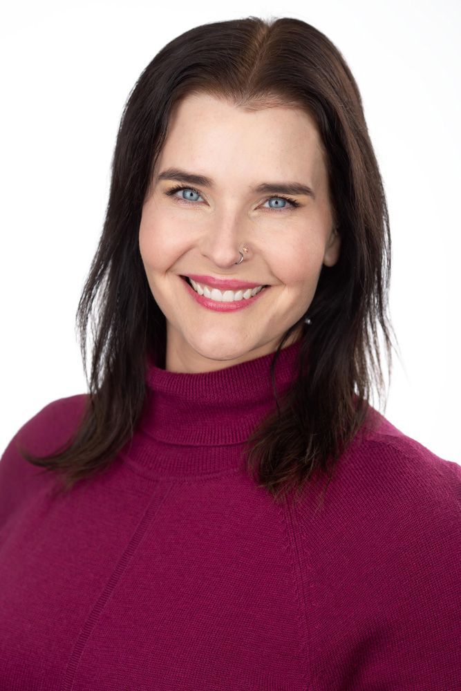 Woman with blue eyes and dark hair smiles, wearing a purple sweater.