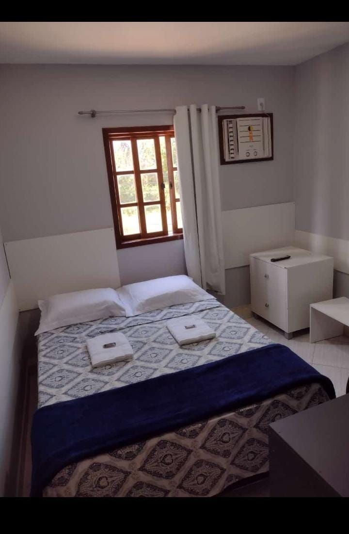 Um quarto aconchegante apresenta uma cama de casal com uma colcha estampada em tons de cinza e branco, um caminho de mesa azul-escuro e dois travesseiros brancos.