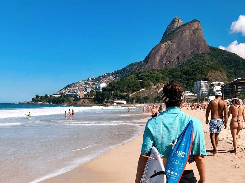 Pessoas caminham pela praia de Ipanema, no Rio de Janeiro, com os picos do Morro Dois Irmãos ao fundo.