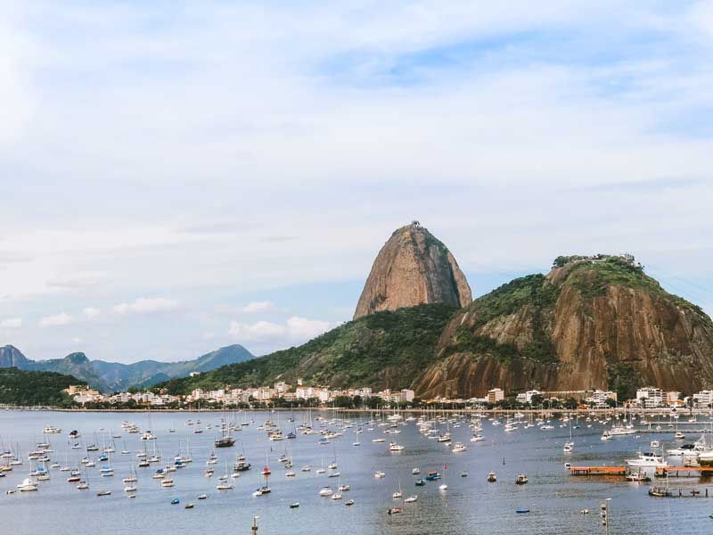 O Monte Sugarloaf ergue-se imponente atrás de uma baía repleta de pequenos barcos sob um céu azul claro.