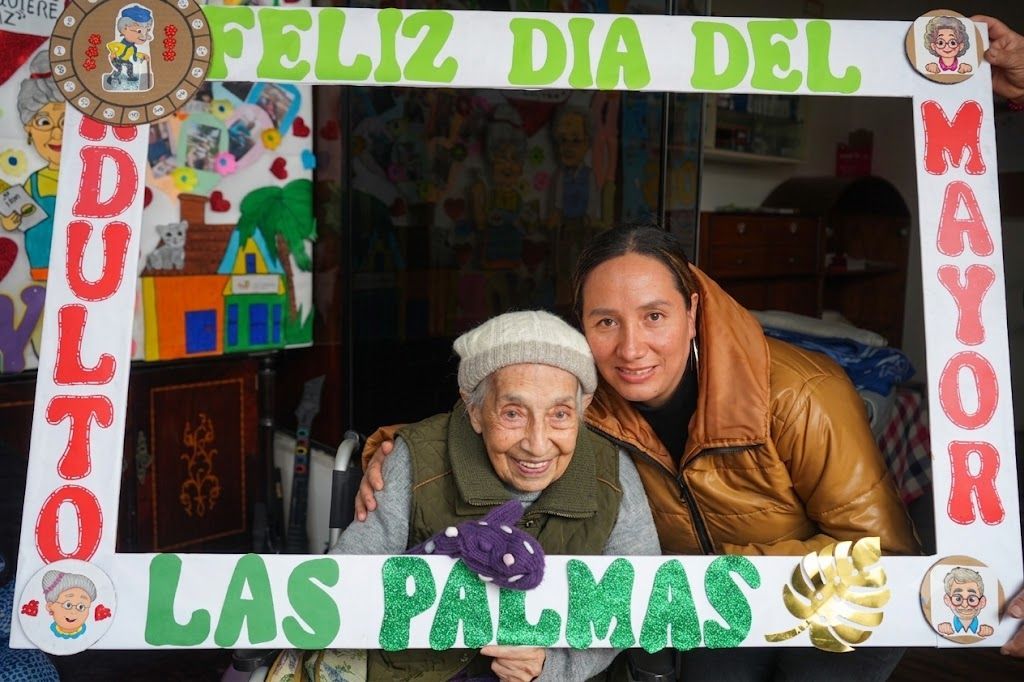 Madre y anciana posando en un colorido marco del Día de la Madre con la inscripción “Feliz Día del de las Palmas”.