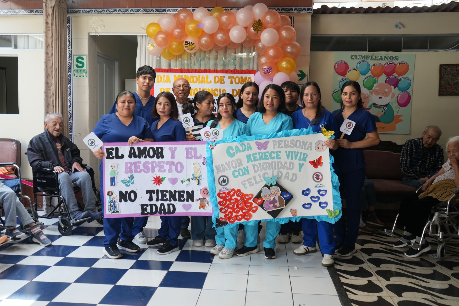 Personas con pancartas de protesta en un evento en interiores con un arco de globos y suelo a cuadros.