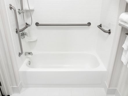 White walk-in bathtub with chrome grab bars, showerhead, and towel rack in a tiled bathroom.