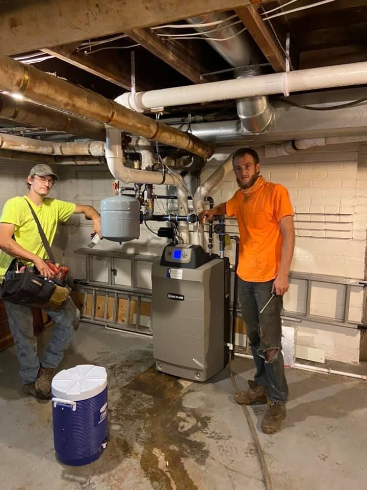 Technicians installing residential HVAC boiler system in basement with copper piping and tools
