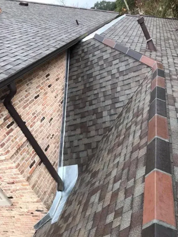 Roof with brown shingles meeting a brick wall; metal flashing and gutter.