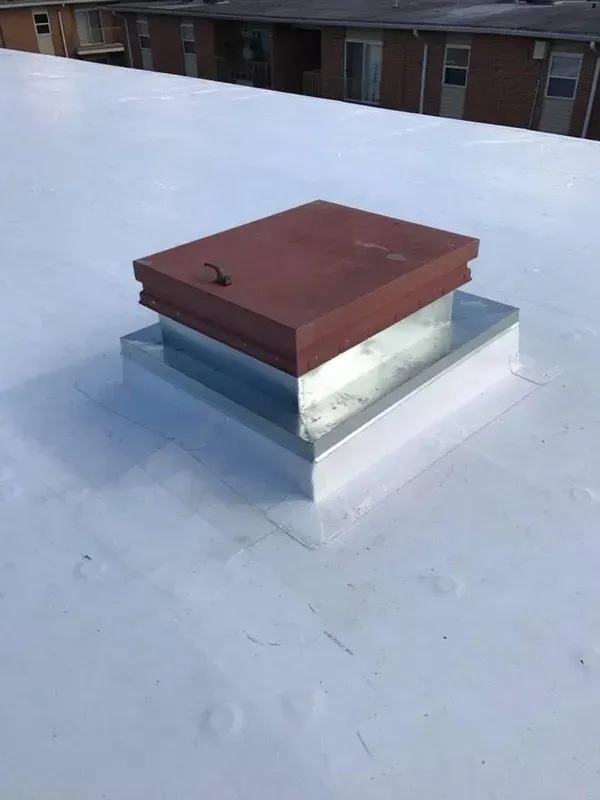 A closed roof hatch with a red cover and a metal base on a white flat roof.