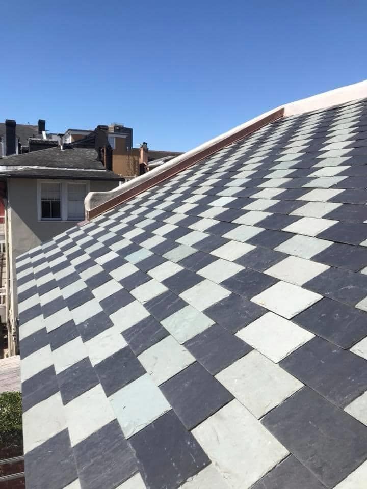 Chessboard-patterned slate roof against a blue sky, with surrounding buildings visible.