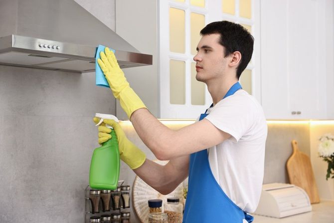 Person cleaning a kitchen range hood with spray bottle and cloth