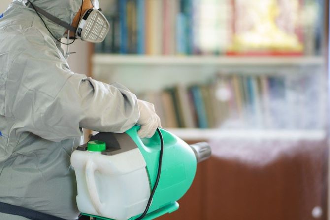 Worker in protective suit spraying disinfectant with a green fogger in an indoor space