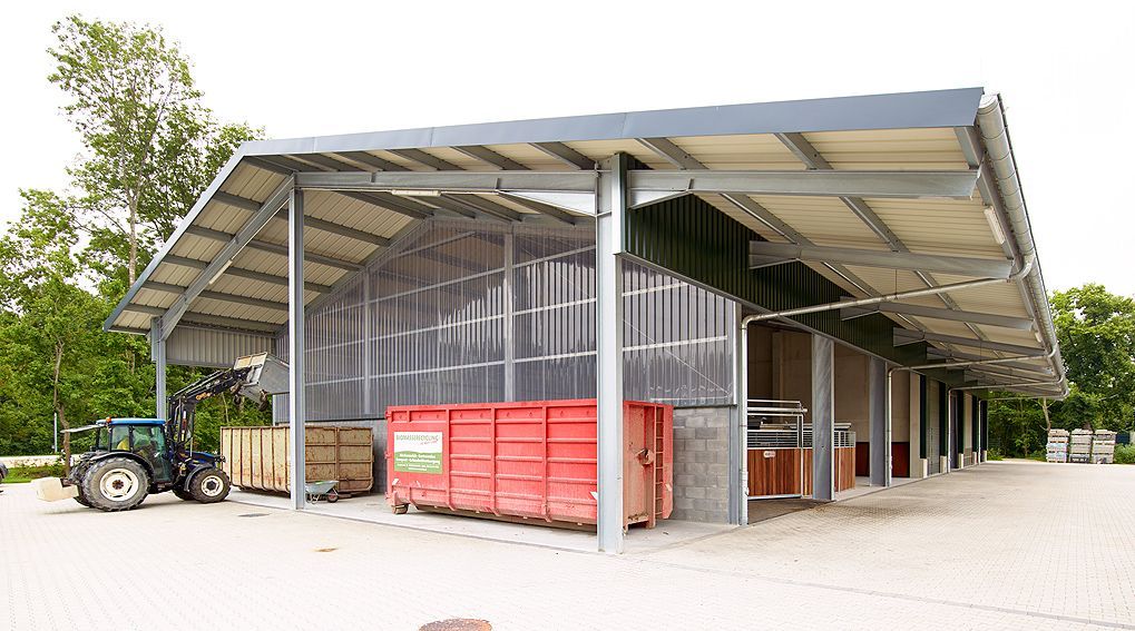 Ländlicher, offener Scheunenschuppen mit Traktor, roten Kisten und im Bau befindlichem Metalldach.