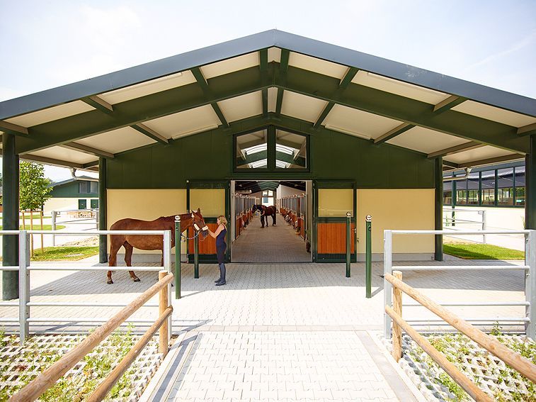 Überdachter Gehweg am Eingang eines Stalls, in dem Pferde stehen, umgeben von einem Geländer.