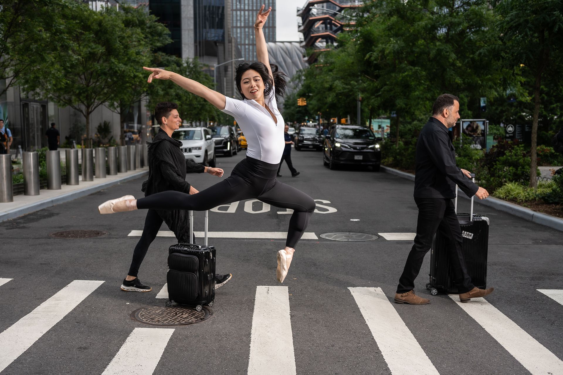 NYC model and ballet dancer Minnie Lee leaping gracefully in midair on a New York City crosswalk wearing pointe shoes and athleticwear, surrounded by photographer Jerry Ghionis
and Melissa Ghionis
— urban elegance and motion.