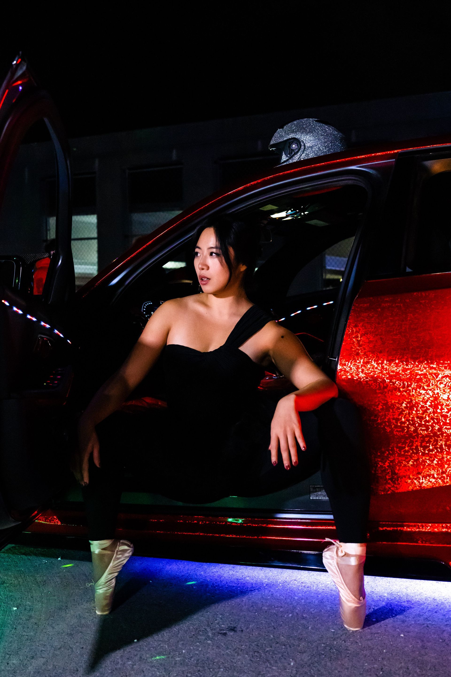 Minnie Lee performing a ballet pose beside a sports car
