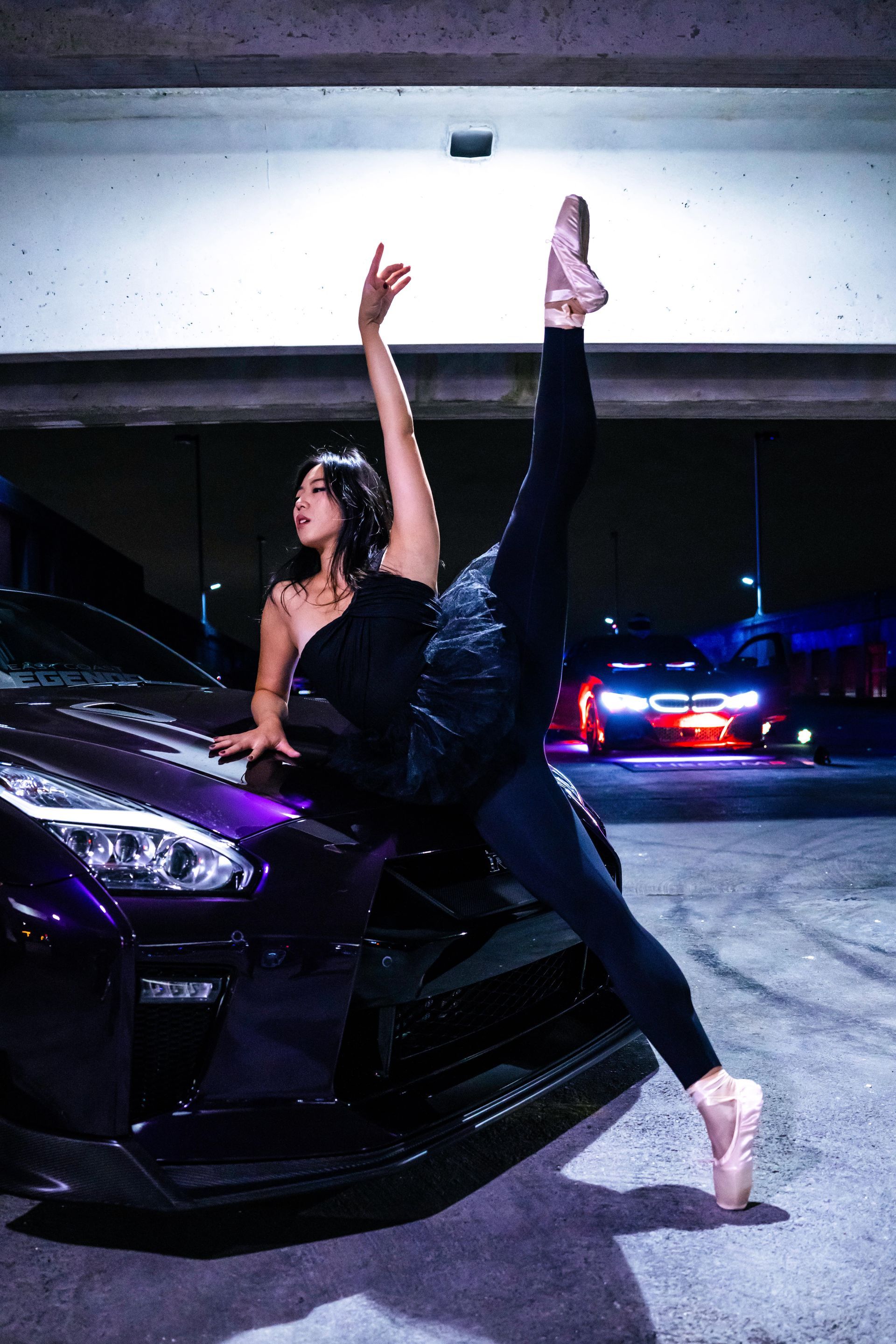 Minnie Lee performing a ballet pose beside a sports car