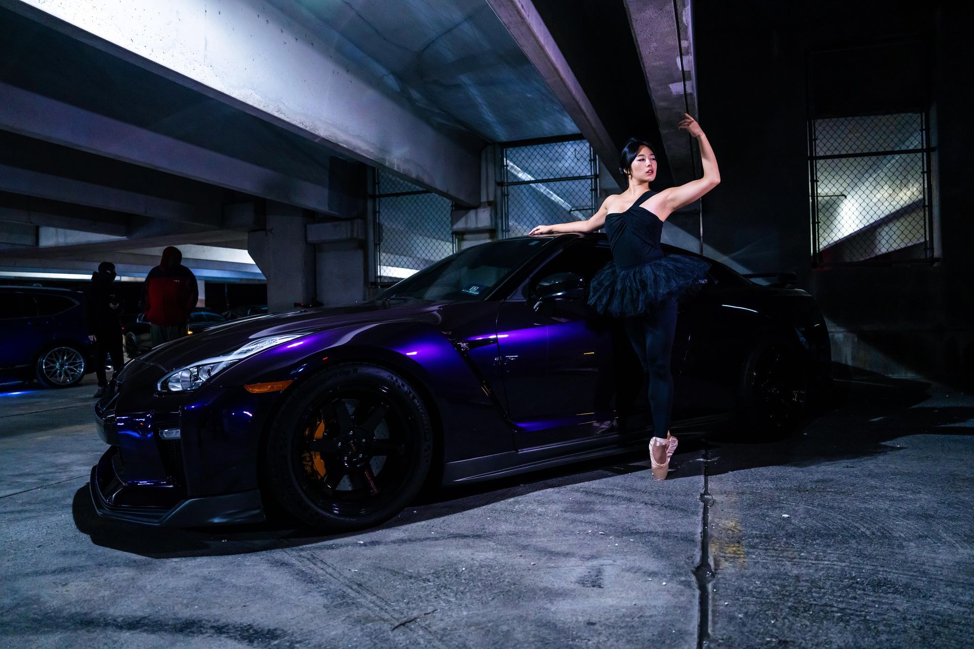 Minnie Lee performing a ballet pose beside a sports car