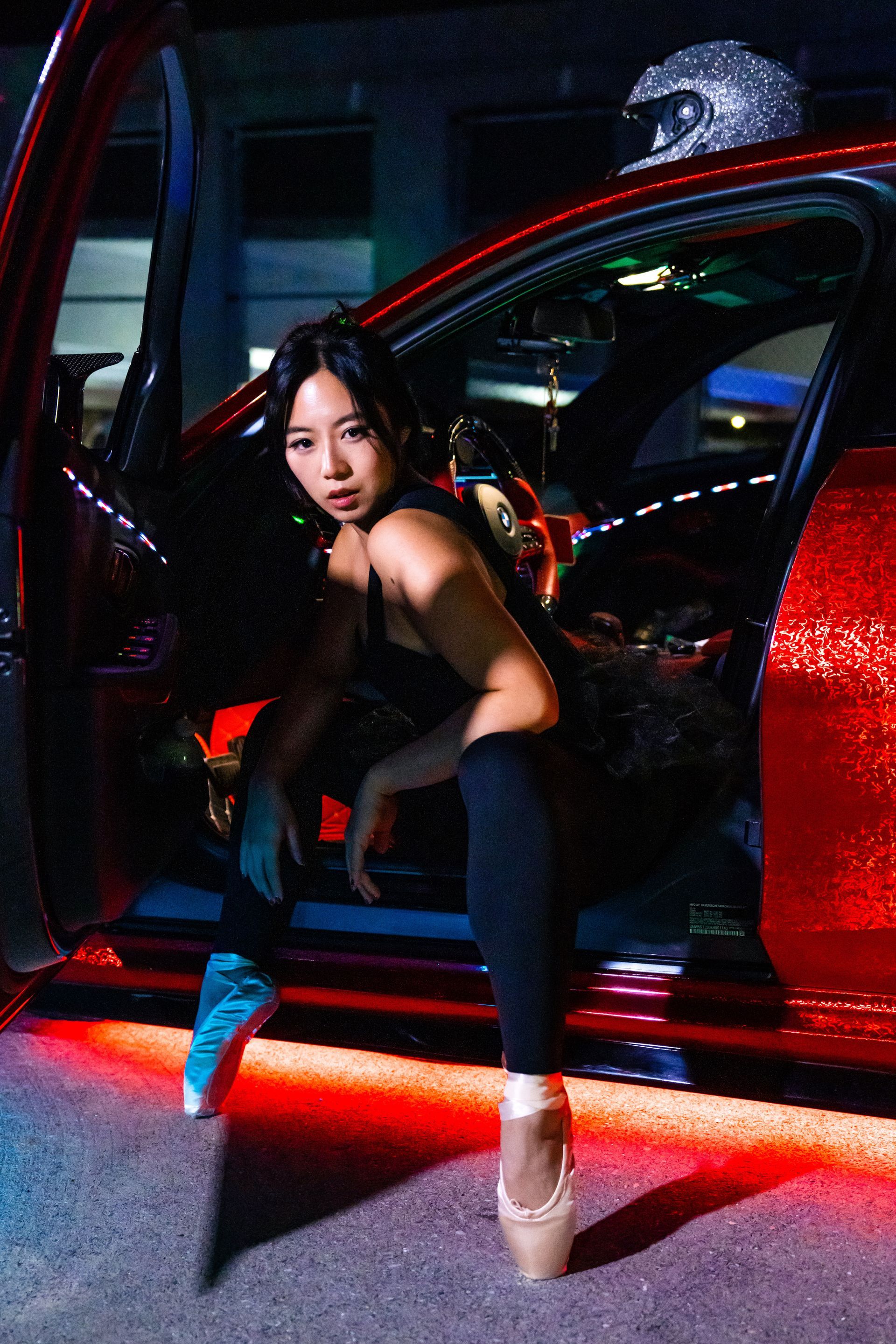Minnie Lee performing a ballet pose beside a sports car
