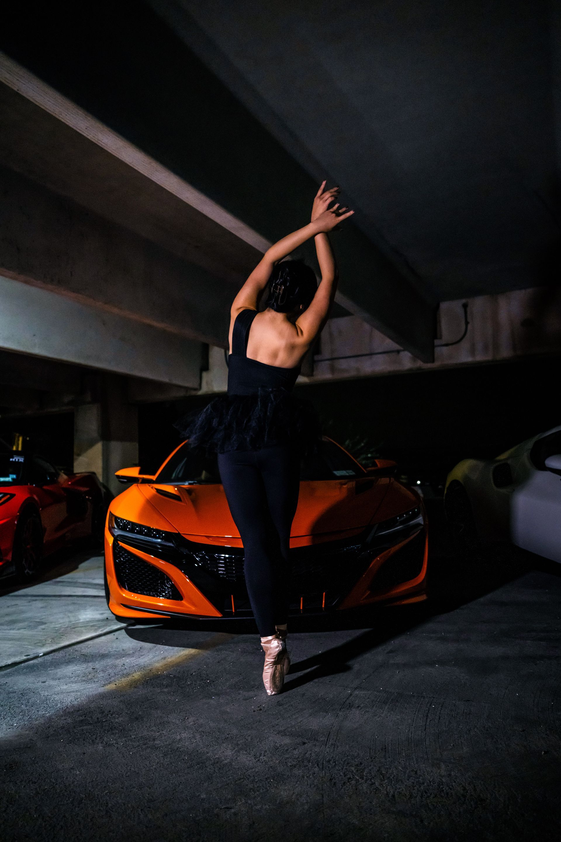 Minnie Lee performing a ballet pose beside a sports car