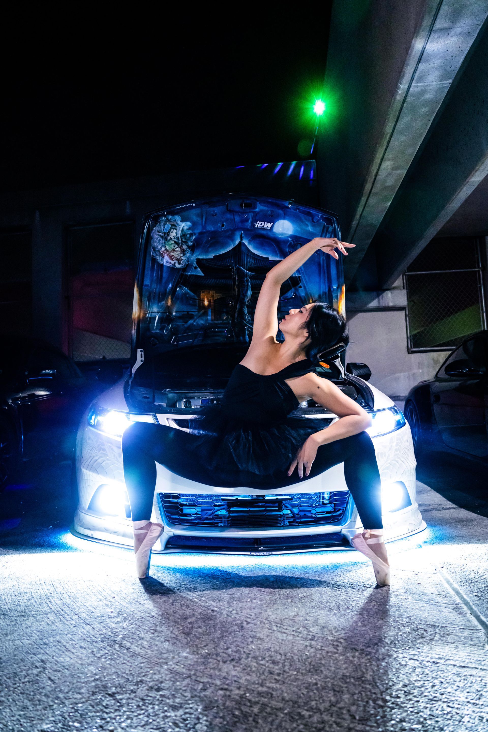 Model Minnie Lee performing a contemporary ballet pose en pointe in front of a customized Cu2 2010 Acura TSX car with illuminated hood art, photographed by 
Josanna Uy at the Checkm8 car meet in NYC.