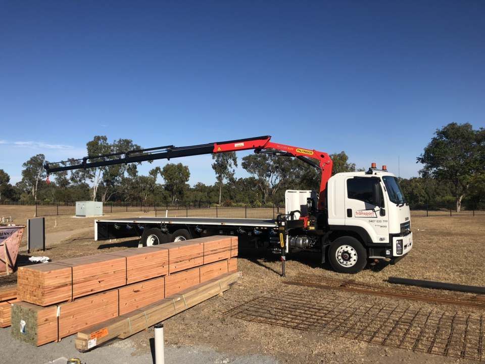 A White Truck with A Crane Is Parked on A Construction Site, Lifting Wooden Beams — J & M Transport Plus in Yeppoon, QLD