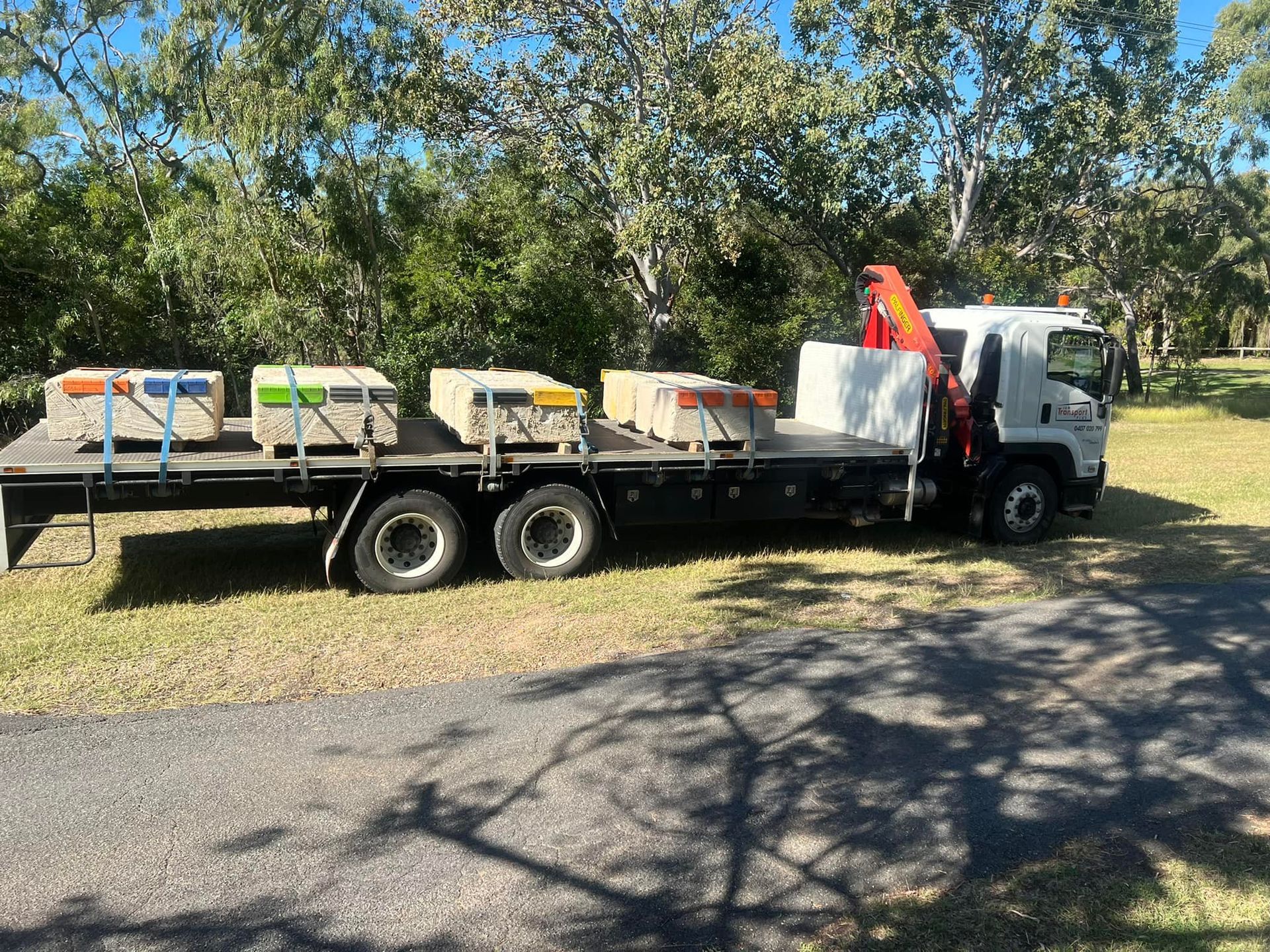 Flatbed Truck Carrying Concrete Blocks in A Grassy Area, Crane Extended — J & M Transport Plus in Barmaryee, QLD