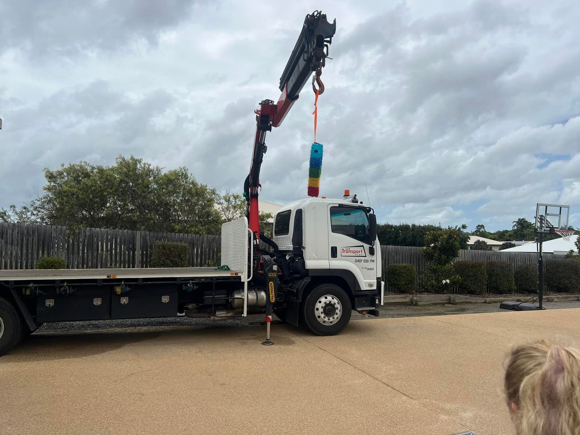 A Flatbed Truck with A Crane Lifting a Colourful Item Against a Cloudy Sky — J & M Transport Plus in Barmaryee, QLD