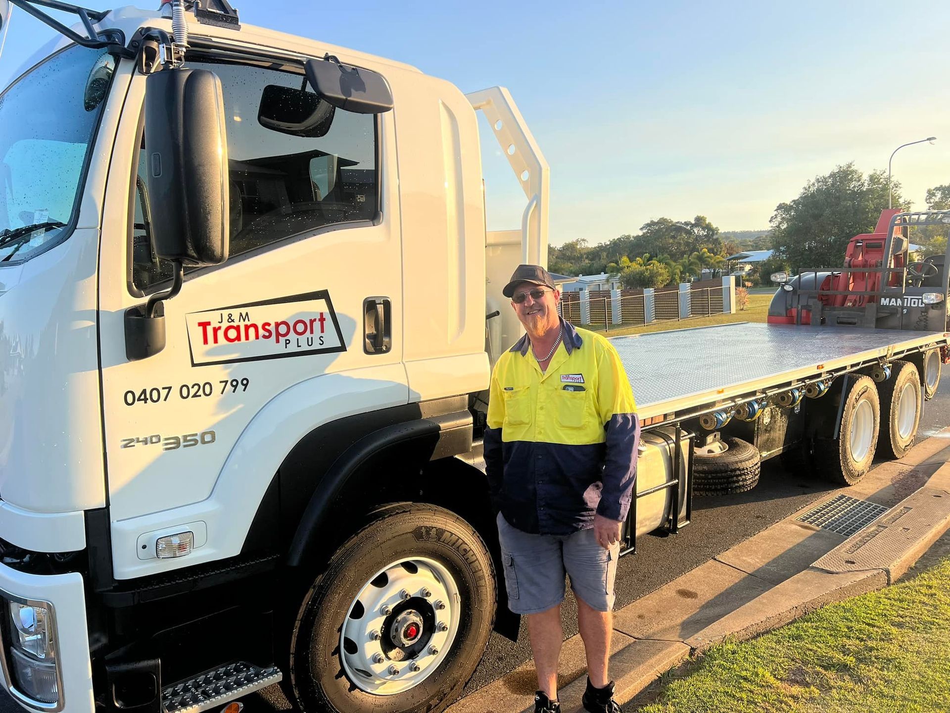Man in Work Attire Standing by A White Flatbed Truck — J & M Transport Plus in Barmaryee, QLD