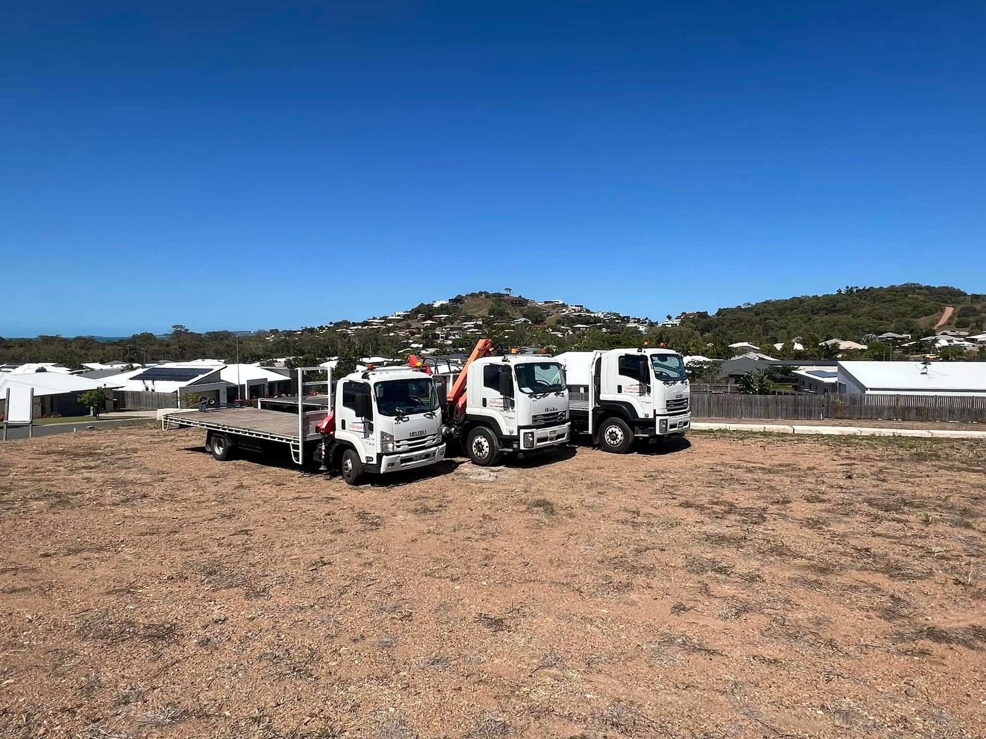 Three White Trucks Parked on A Gravel Lot Under a Clear Blue Sky — J & M Transport Plus in Barmaryee, QLD